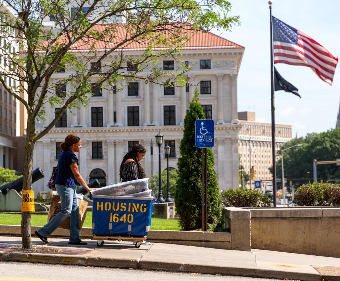 people pushing moving cart through campus